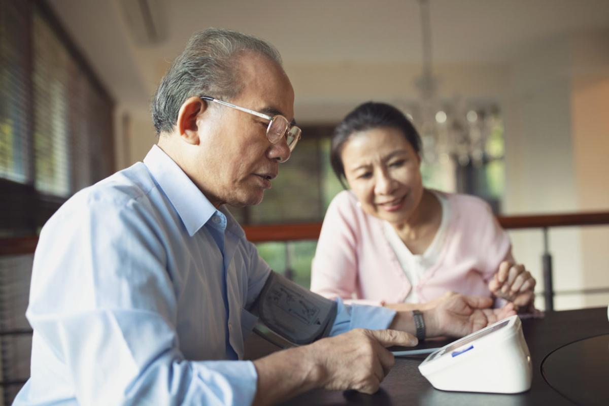 Asian couple in their home, the man is checking his blood pressure.