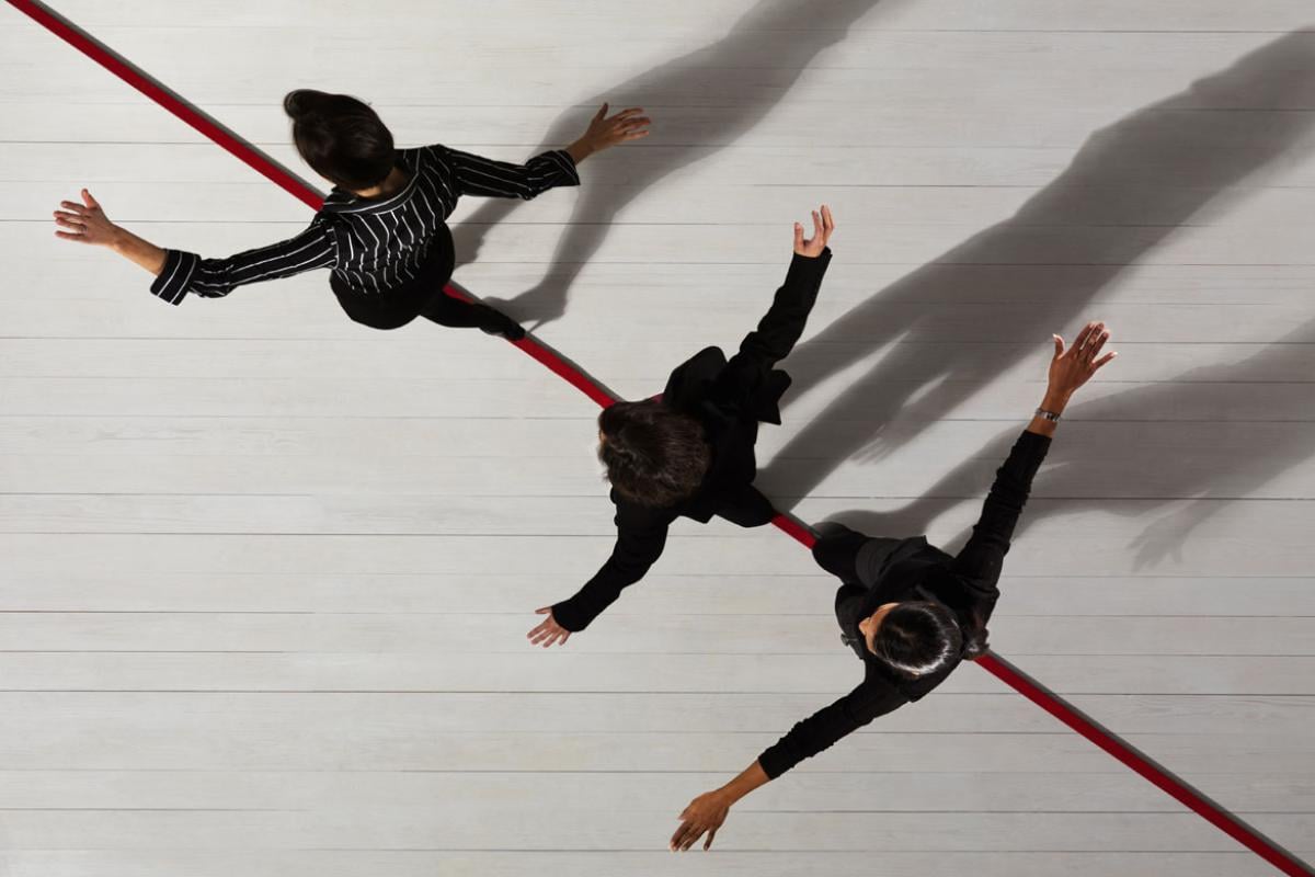 Photo-illustration looking down on three people walking a red line representing a tight rope.