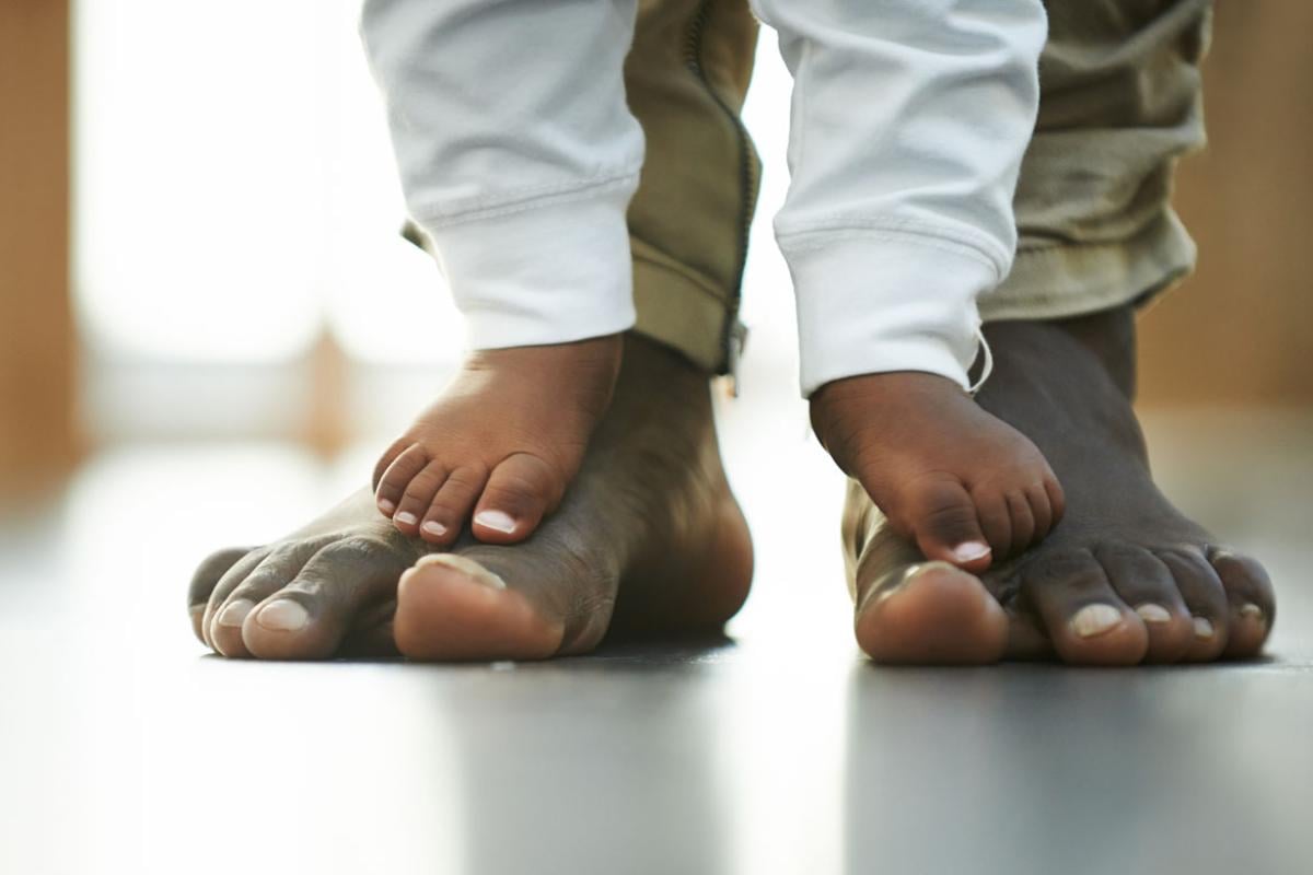 Close-up of an African-American parent's feet with their child's feet on top.