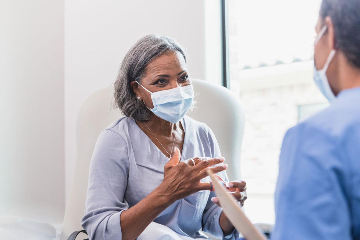 Woman patient with mask talking to physician wearing mask