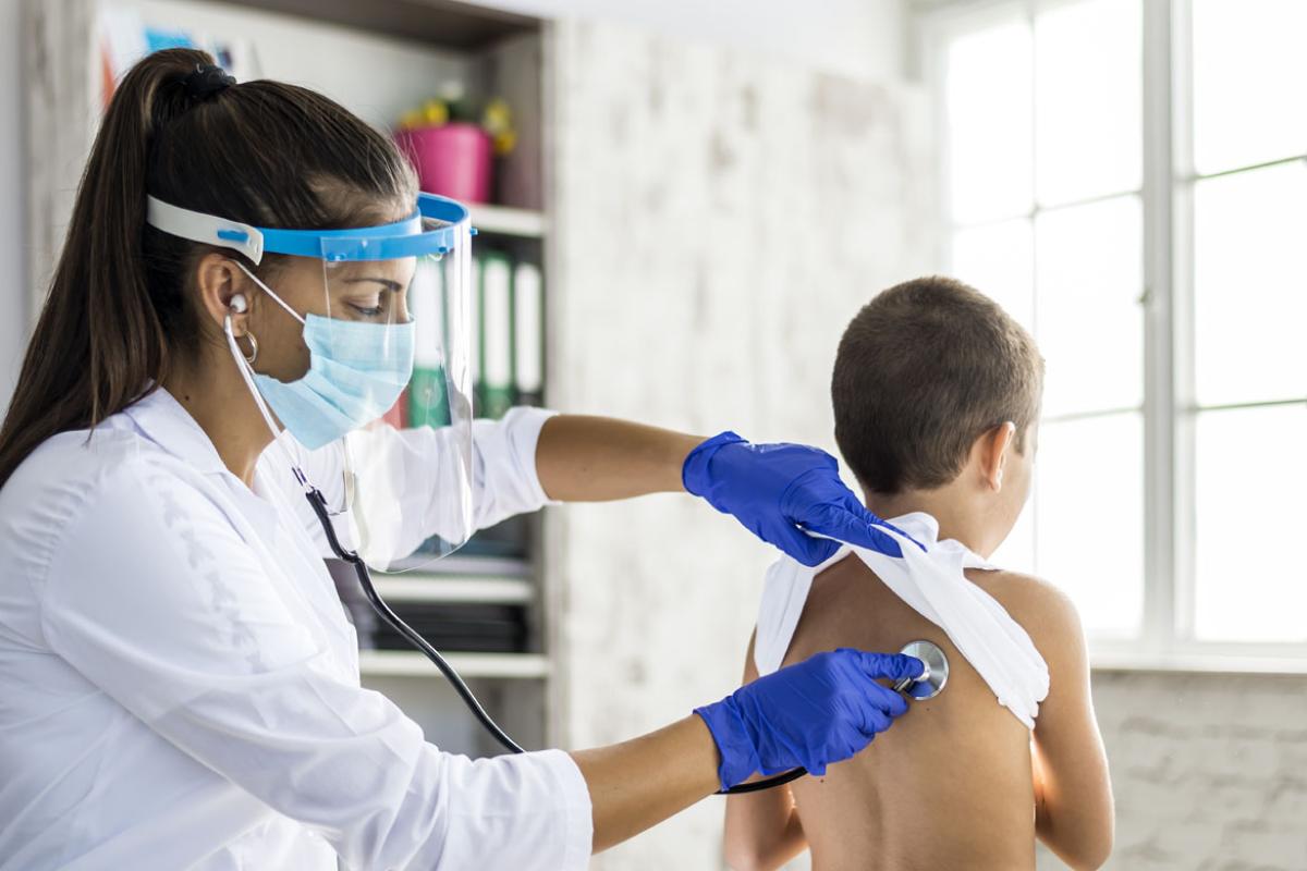 Woman physician with PPE and stethoscope examining child patient