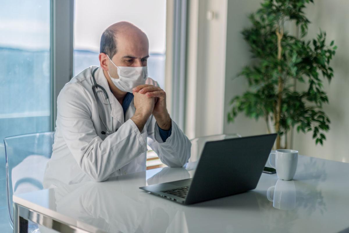 Physician wearing a mask and sitting at a desk looking at laptop screen