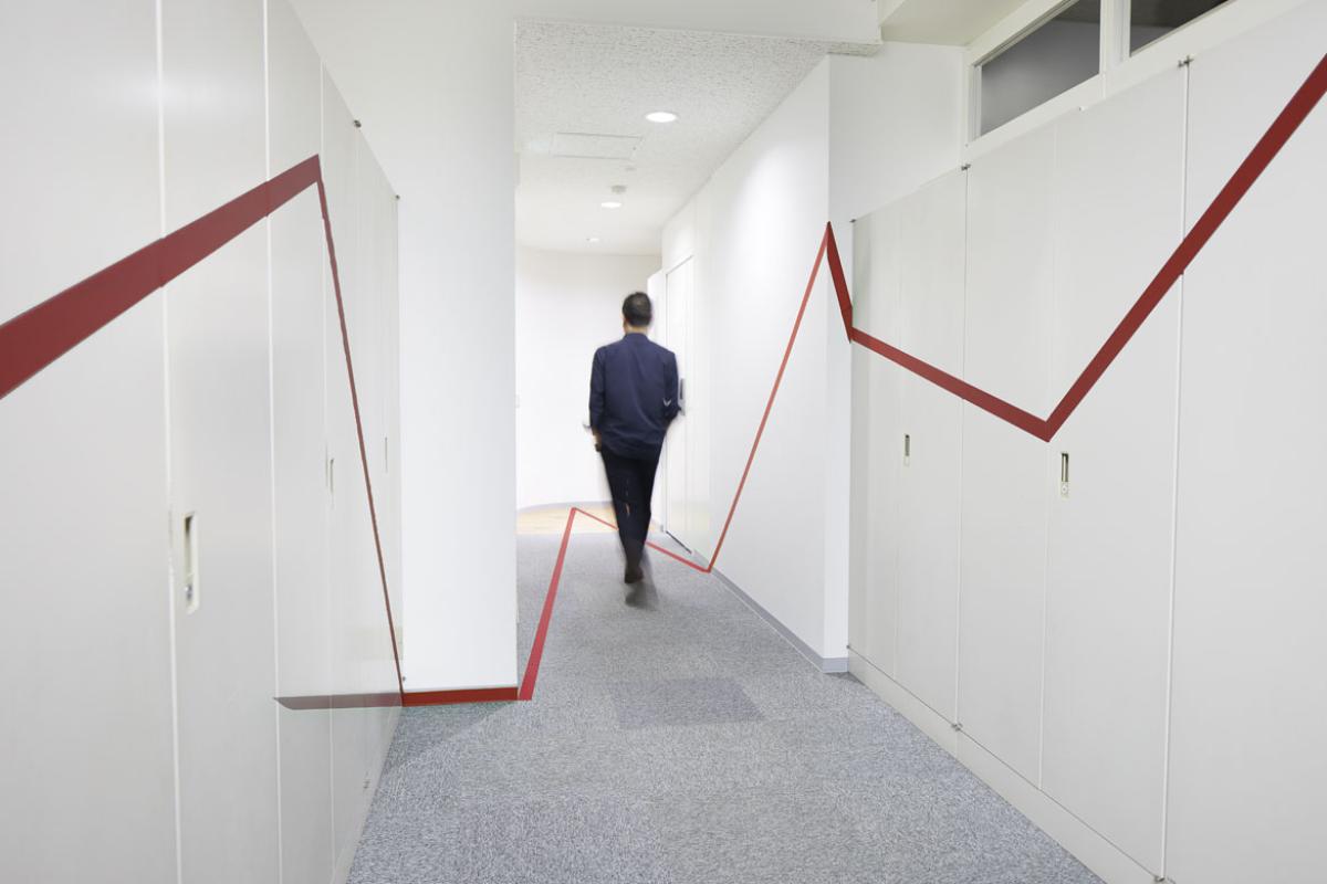 Person in blue suit walking down empty hallway and walls with a red stripe on each side.