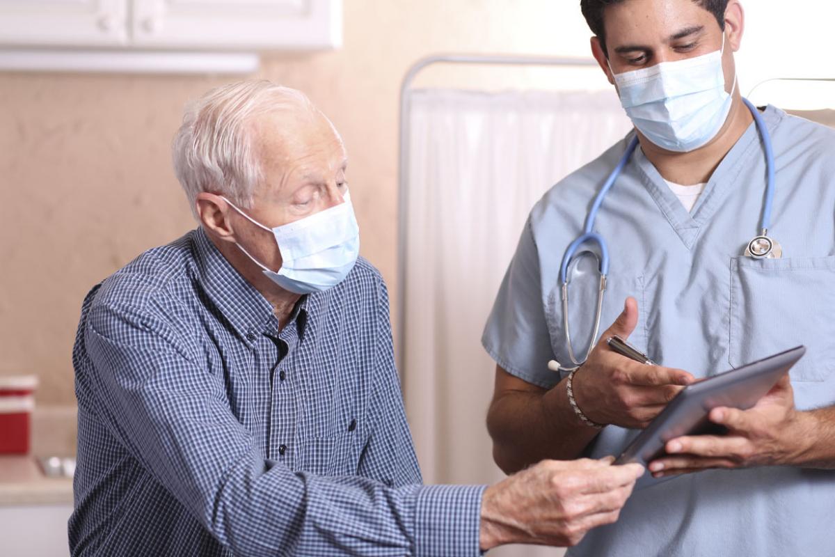 Physician and patient wearing masks and reviewing information on a tablet.