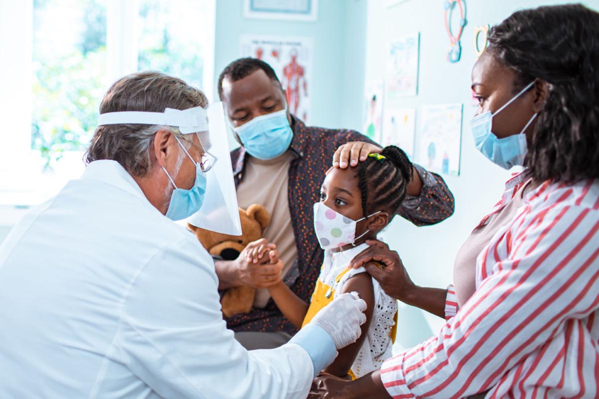Doctor treating an young African-American patient as her parents look on.