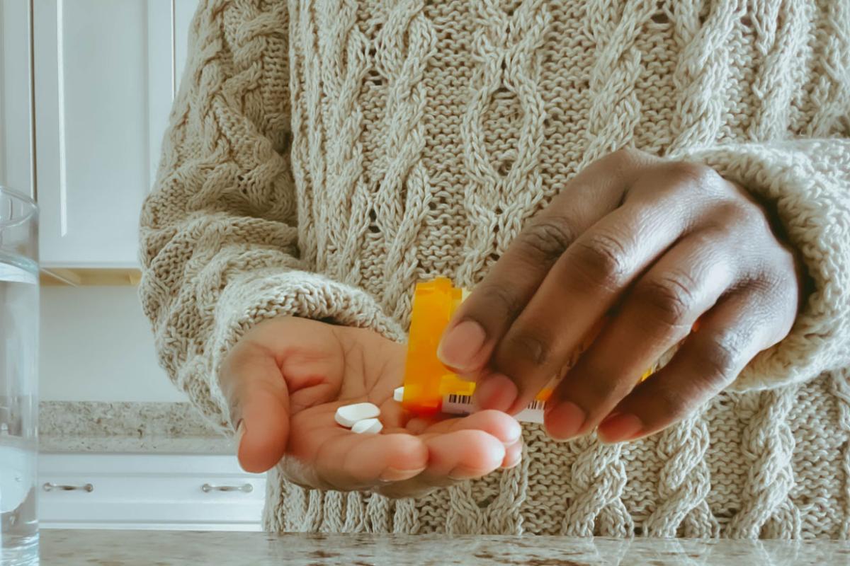 Close up of an African-American pouring out pills from a prescription bottle.