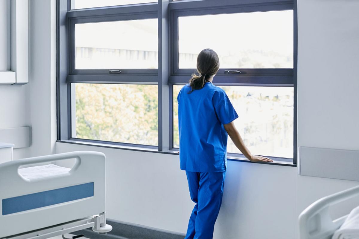Doctor in scrubs looking out the window of an empty hospital room.