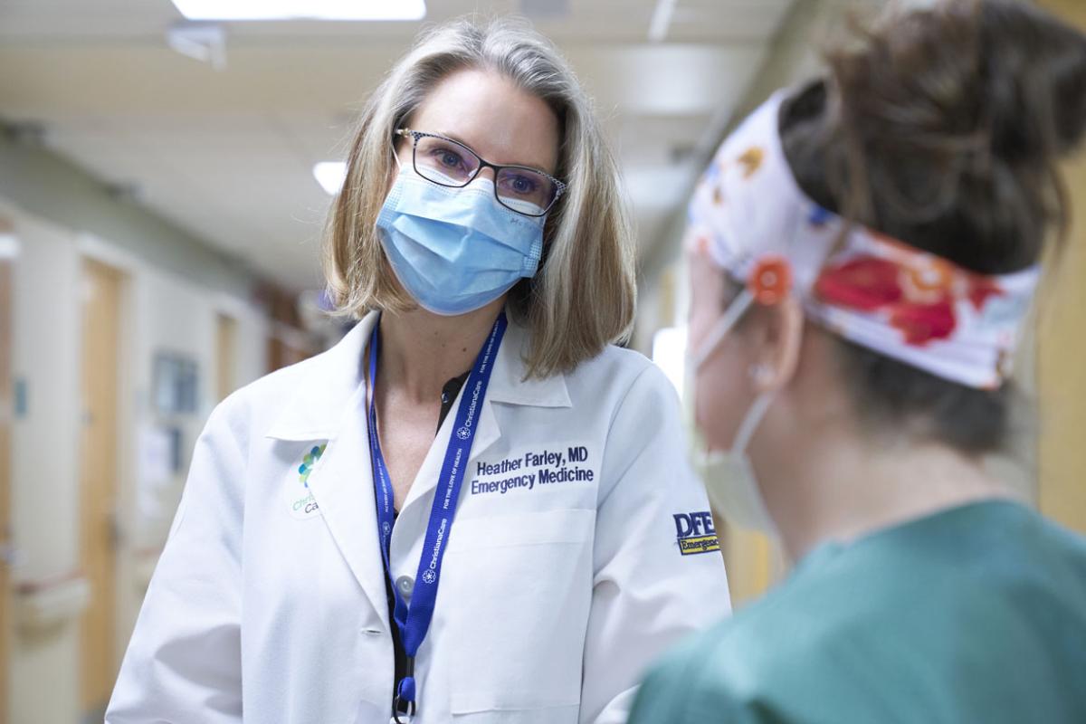 Heather Farley, MD, in a mask speaking to a woman in PPE and scrubs.