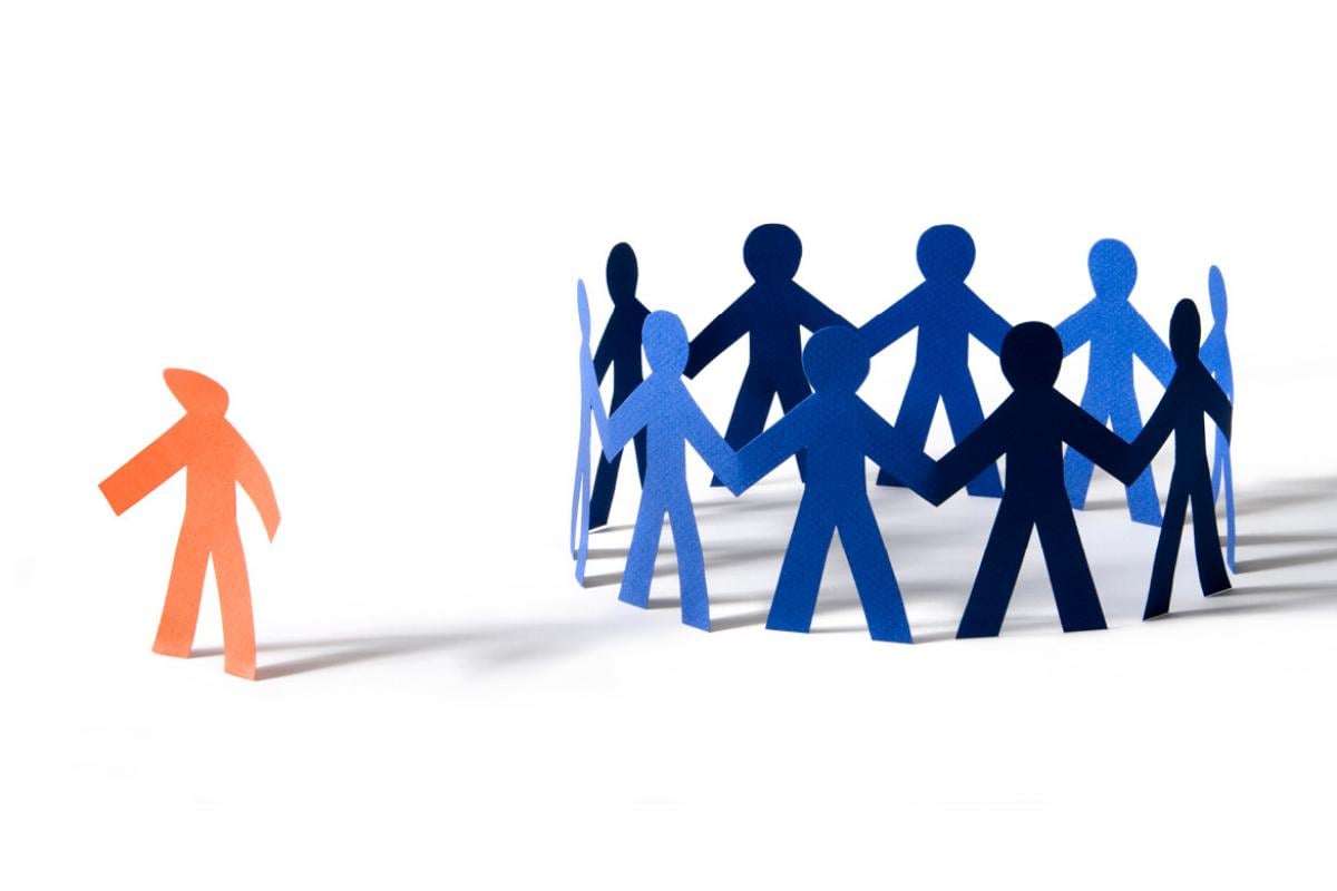  Orange paper person with dejected stance off to the side of a circle of blue paper people