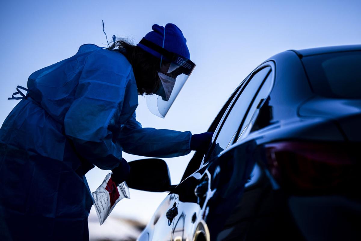 Health care professional in PPE standing outside of a car