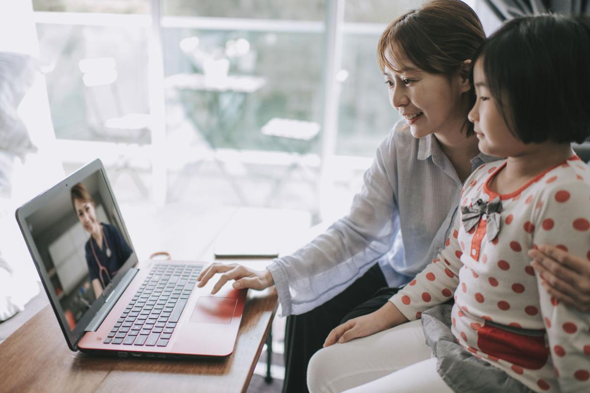 A mother and daughter speaking to a doctor remotely by laptop.
