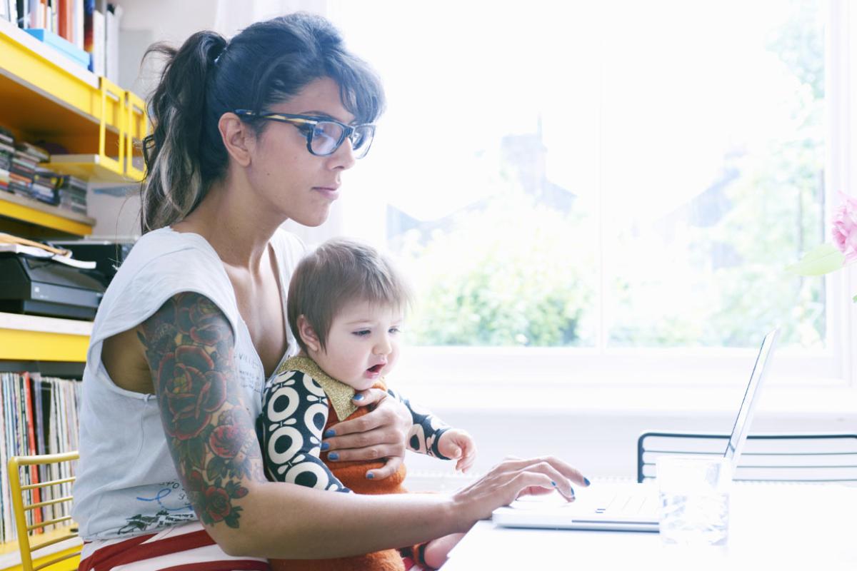 Person holding an infant and working on a laptop
