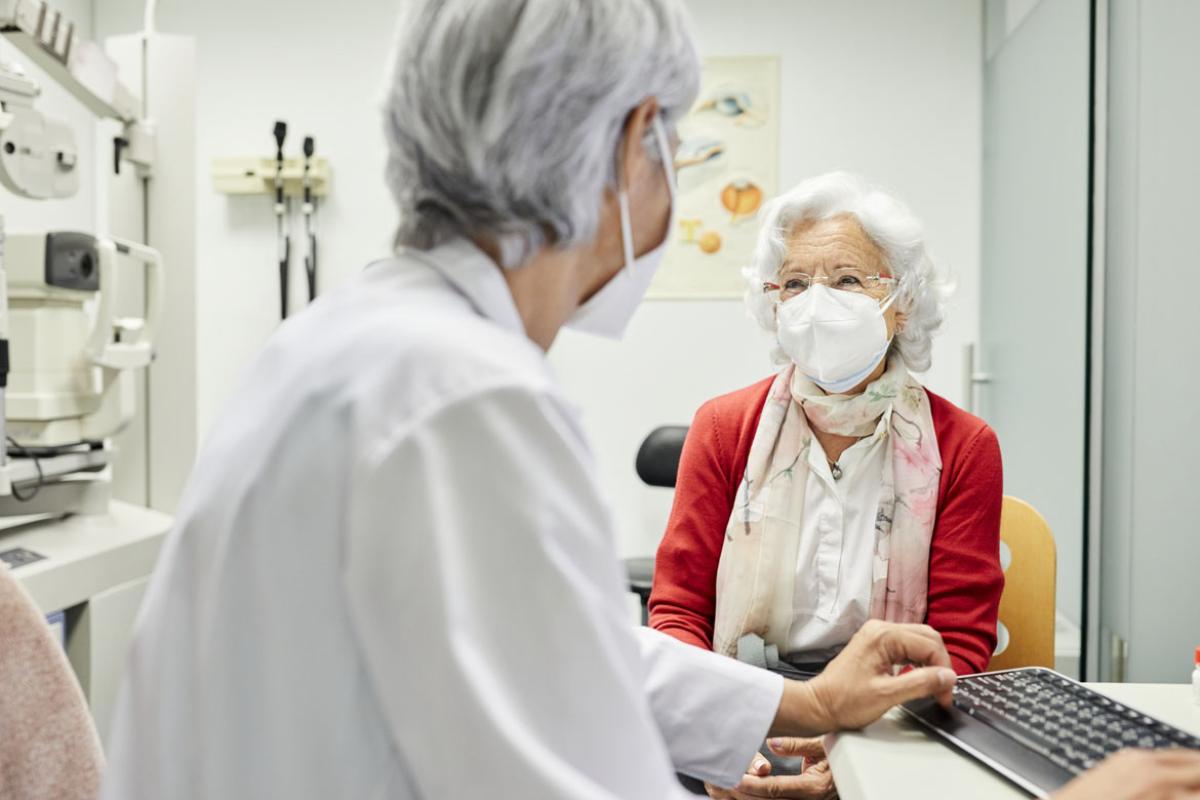 Patient sitting at desk consulting with physician, both wearing masks