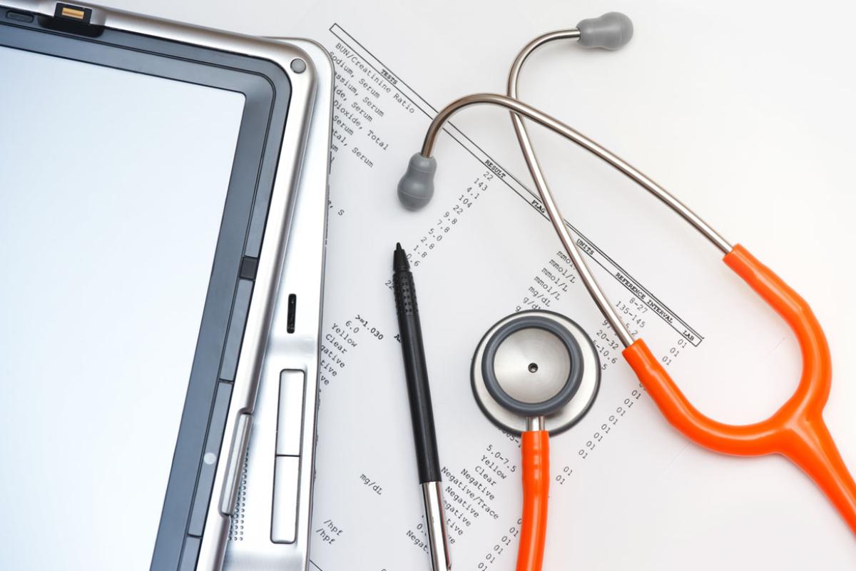 A stethoscope, stylus, two PDA tablets, and a printout stacked on a white background.