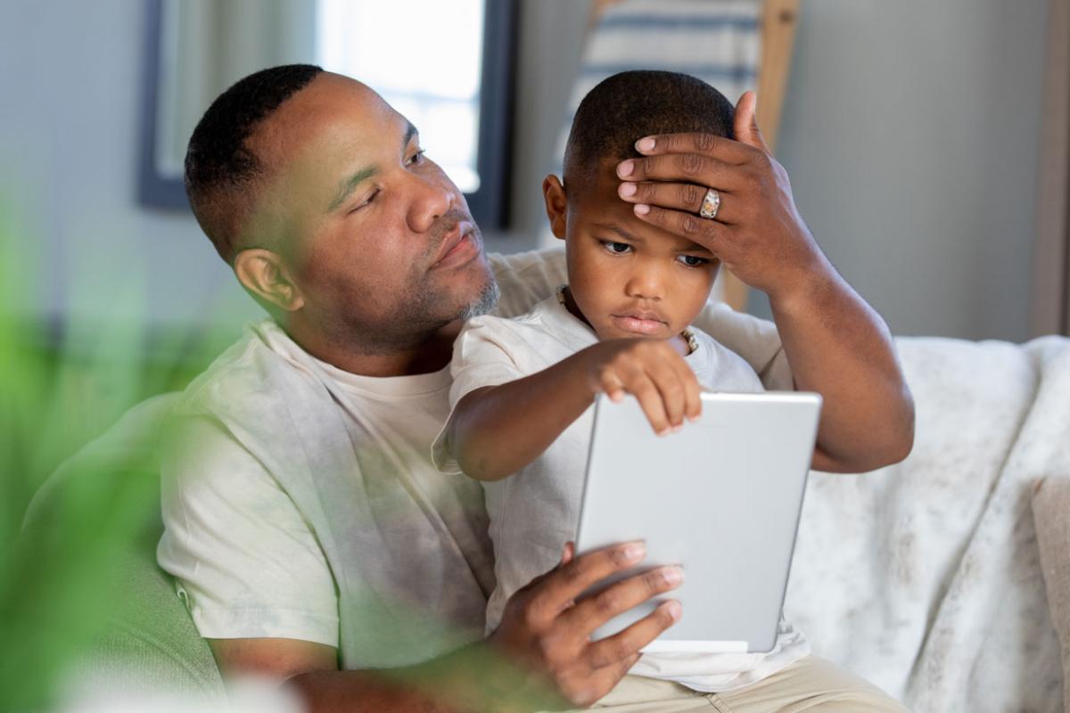 Father checking his young son's forehead for temperature, while holding a tablet.