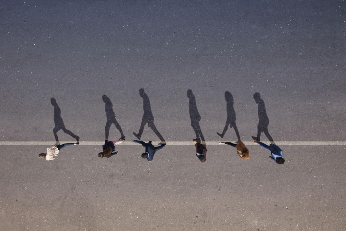 People walking in line with their shadows on asphalt.