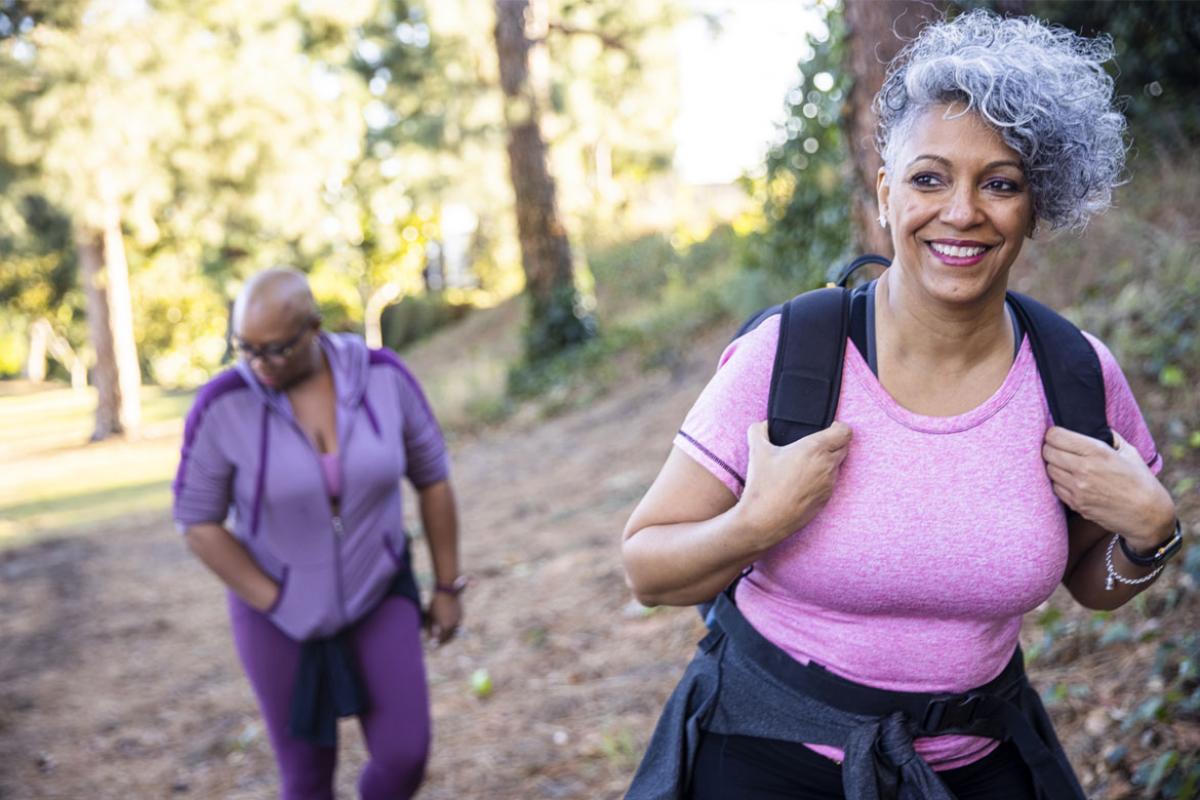 A photo of an African-American couple taking a walk in the woods, with the woman smiling in the foreground and the man slightly out of focus in the background.