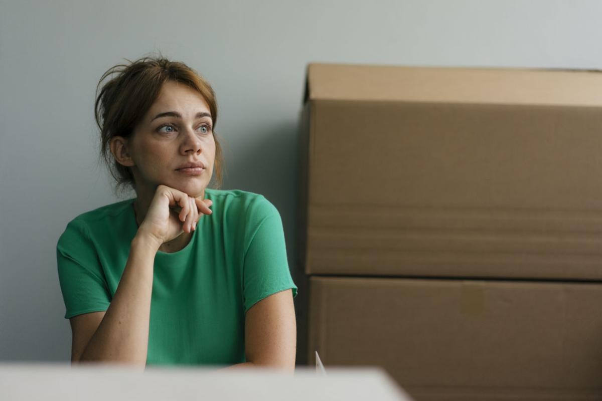 A woman, looking distressed, sitting in front of moving boxes.