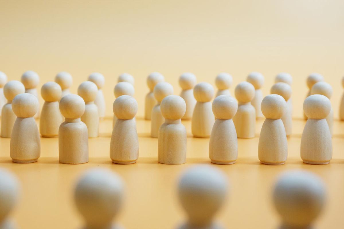Three rows of wooden figures standing in the background with a blurry row of wooden figures facing them in the foreground.