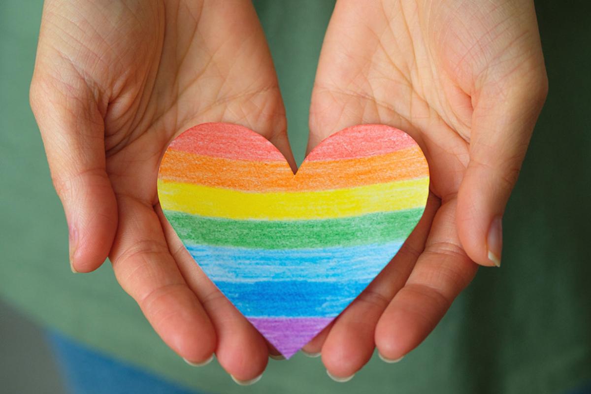 Hands holding a rainbow paper heart.