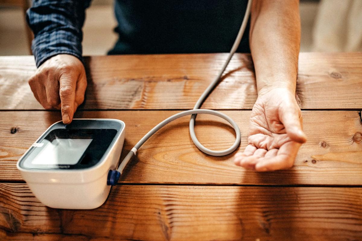 Tight shot of person sitting down at a table and using a self-measured blood pressure (SMBP) device.