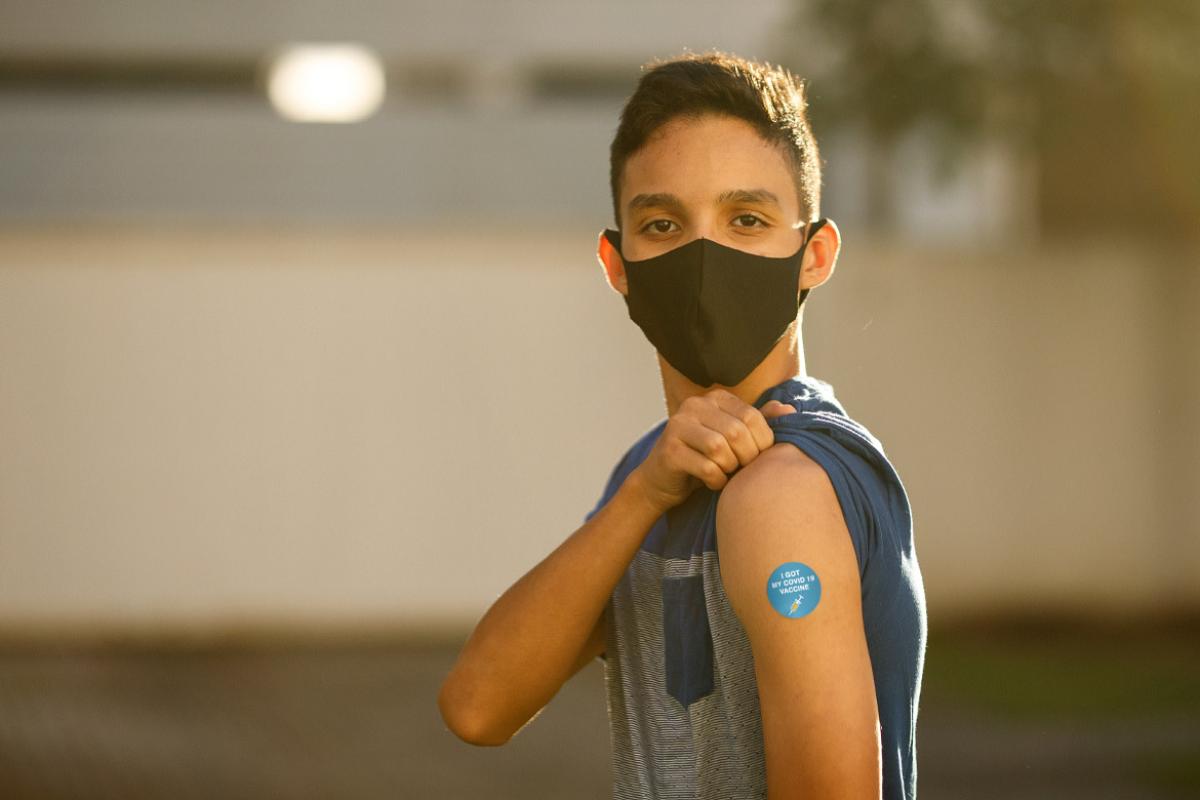 Young man with mask, showing off vaccine shot.