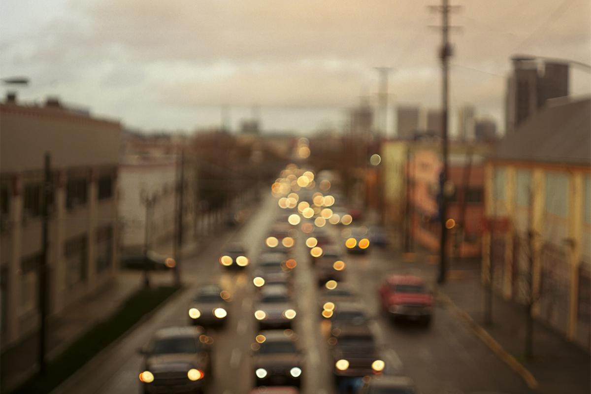A blurred shot of a town street crowded with automobile traffic at dusk.