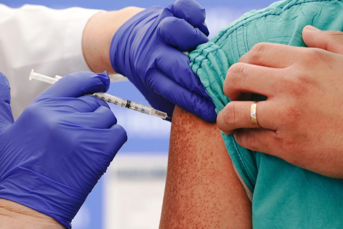 Close up of health professional wearing gloves inoculating person with a vaccine on their right arm.