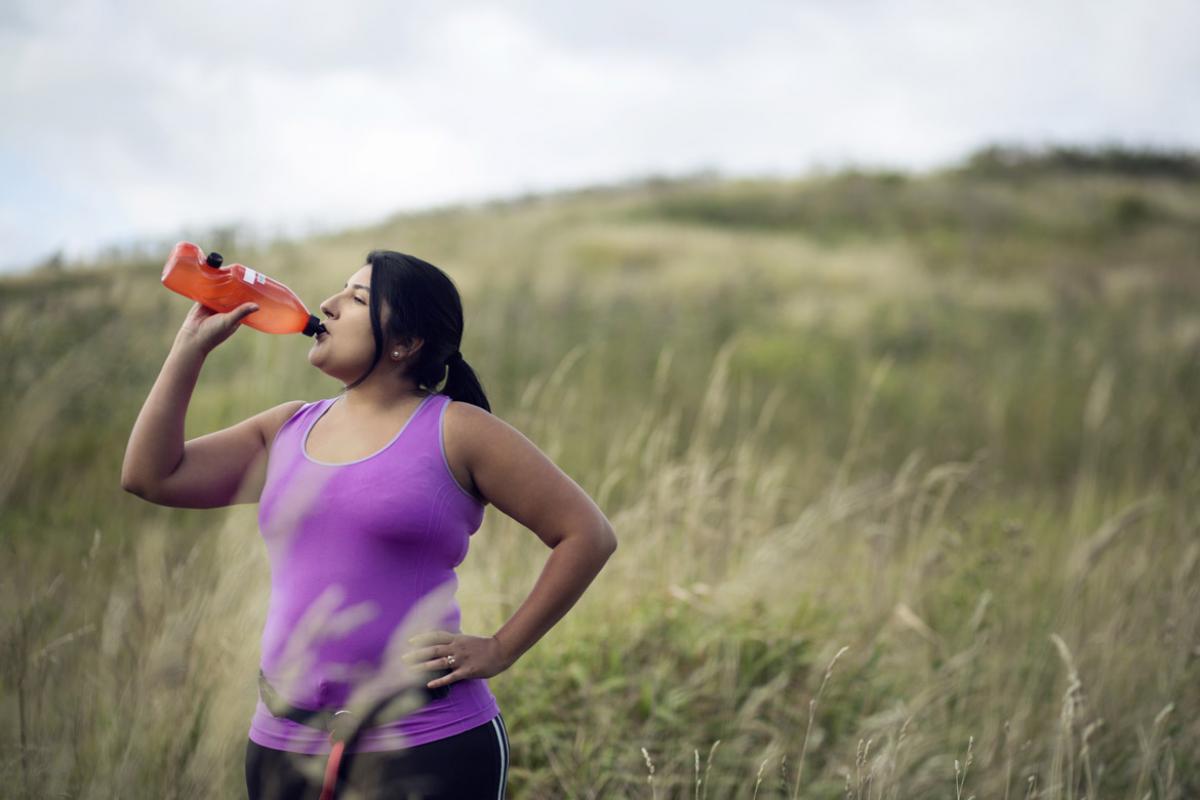 Woman pausing in a field during a hike or walk to take a drink from a bottle of water or an energy drink.