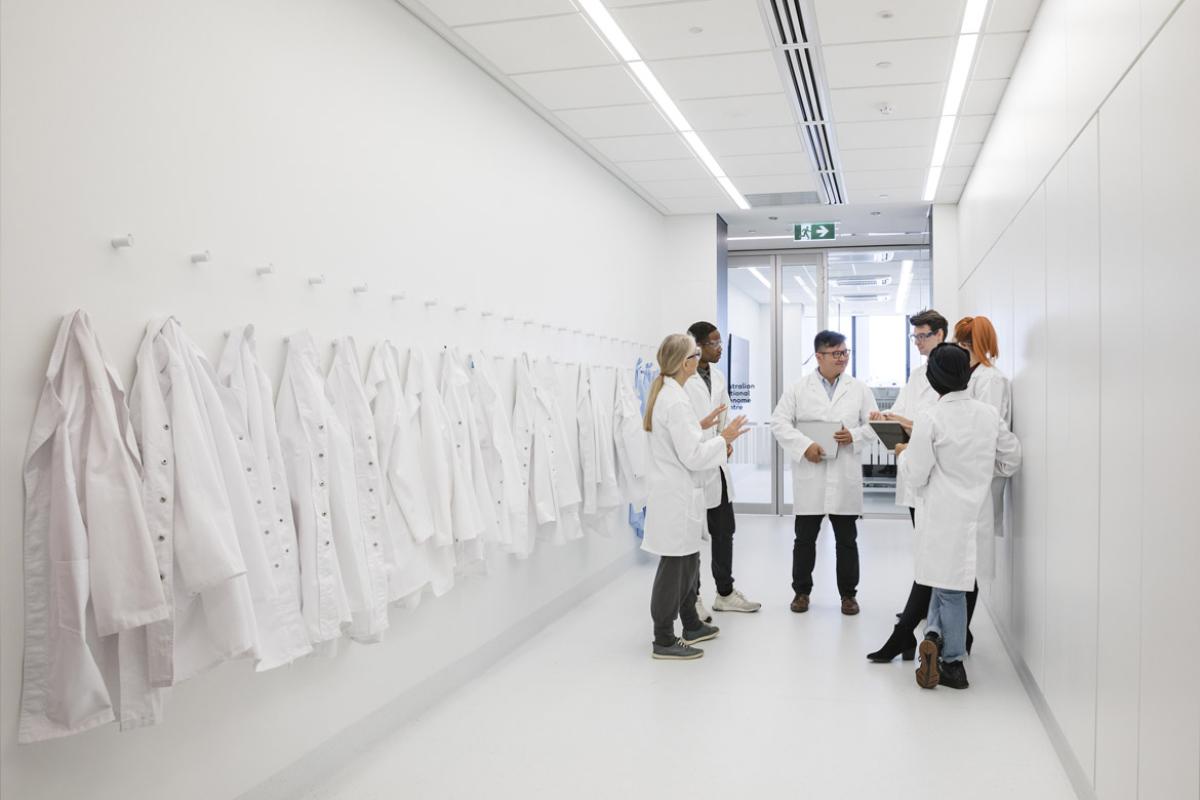 Group of physicians standing in a corridor with white physician coats hanging on racks on a left side wall.