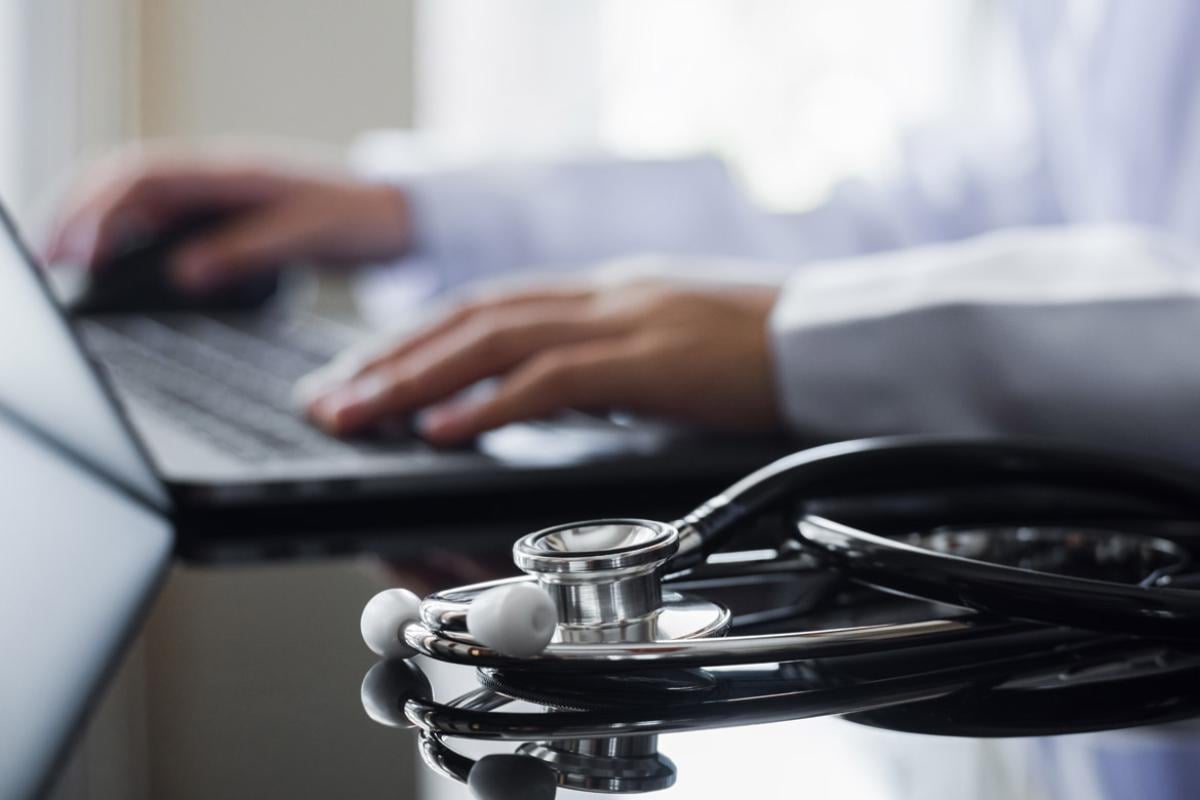 Tight shot of physician working on a laptop with a stethoscope on the side of the desk