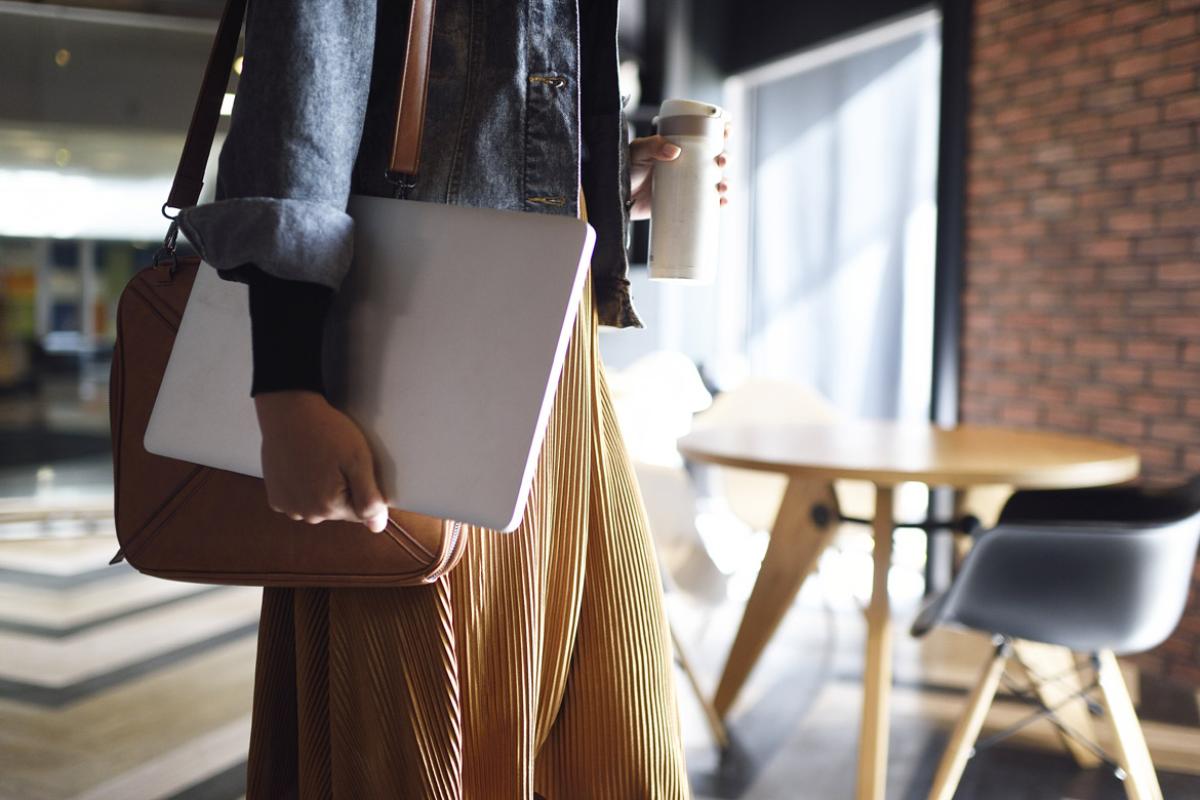Woman carrying laptop, shoulder purse and beverage cup