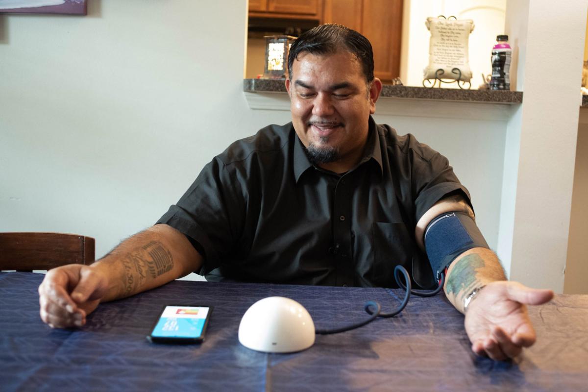 Man using a self-measured blood pressure (SMBP) device with a cell phone on the table.