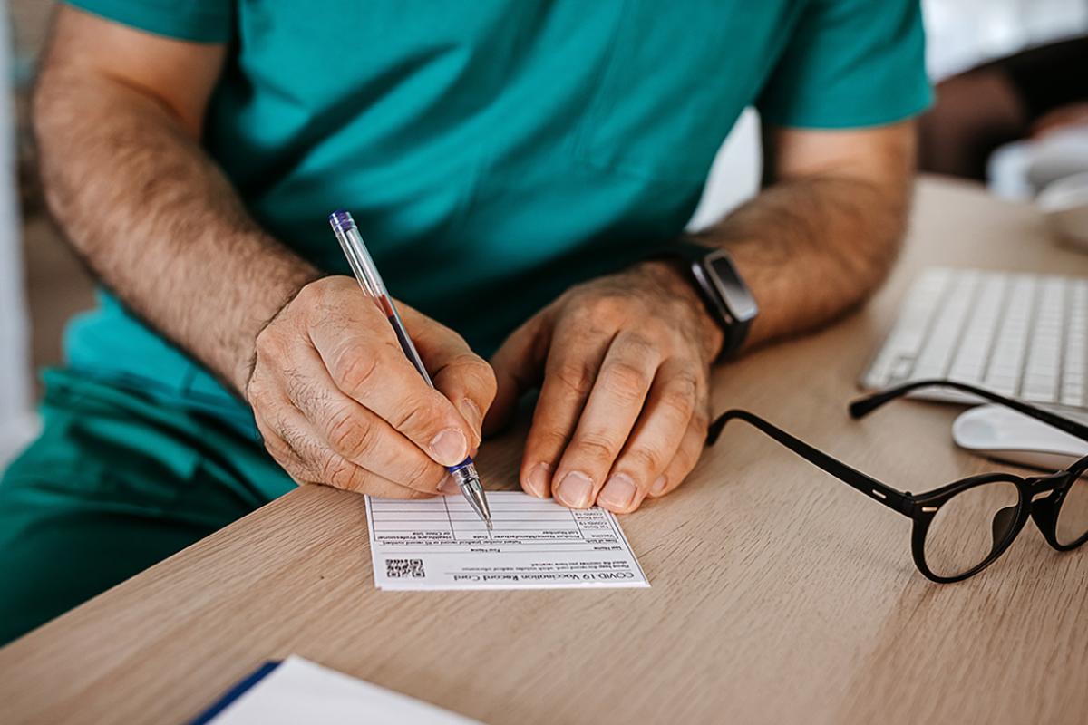 Health care professional sitting down at a desk filling out a vaccine card