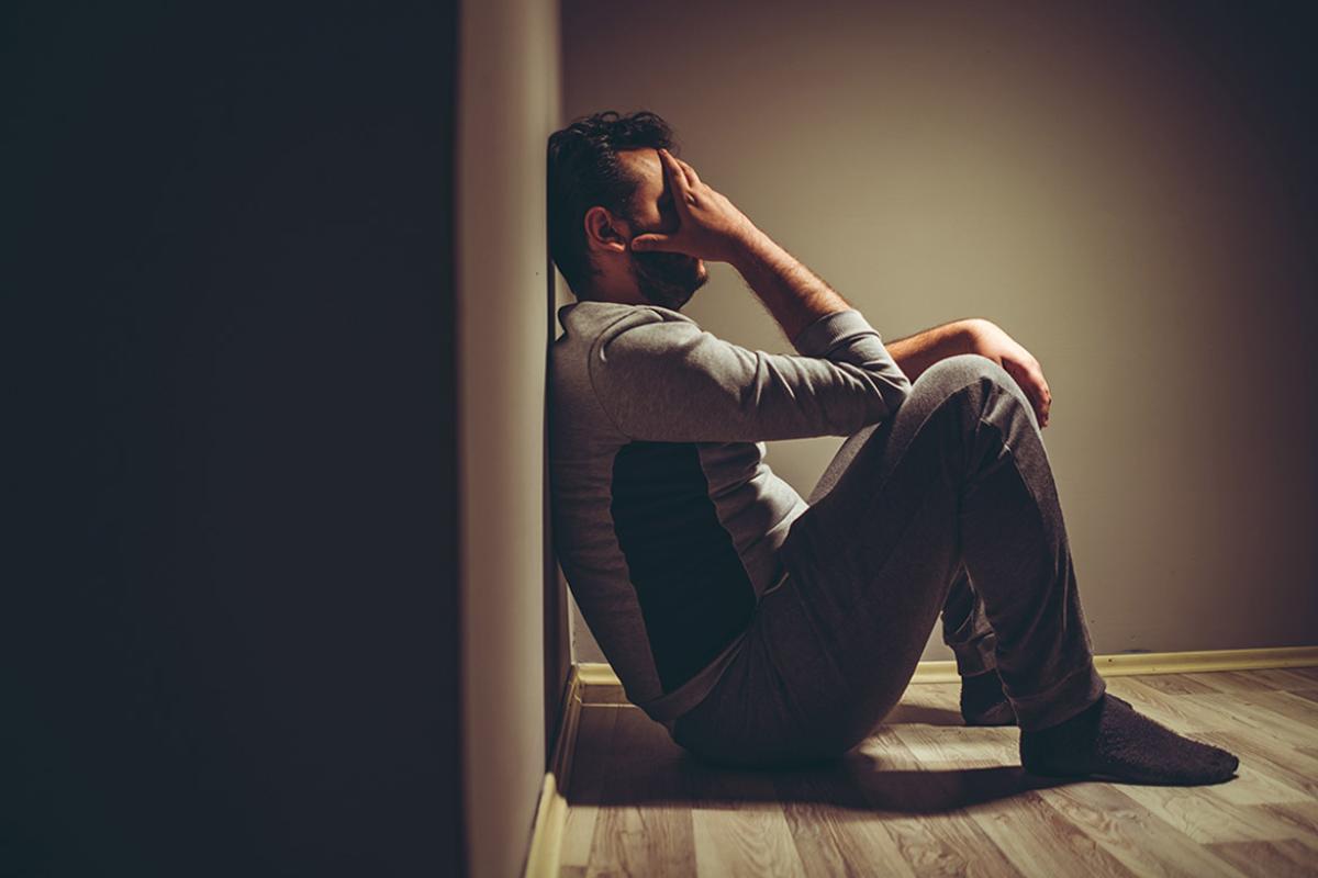 Man sitting on floor against a wall with right hand covering face