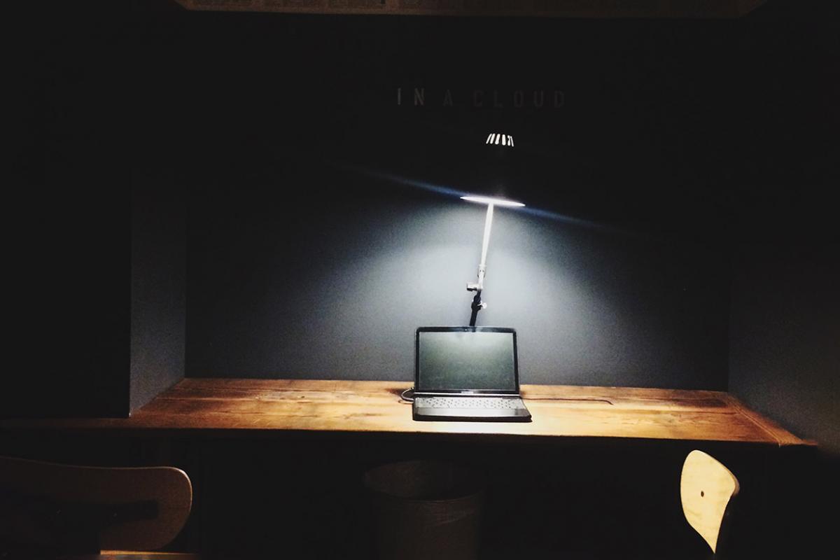 Light from lamp illuminating a laptop on top of desk in a dark room