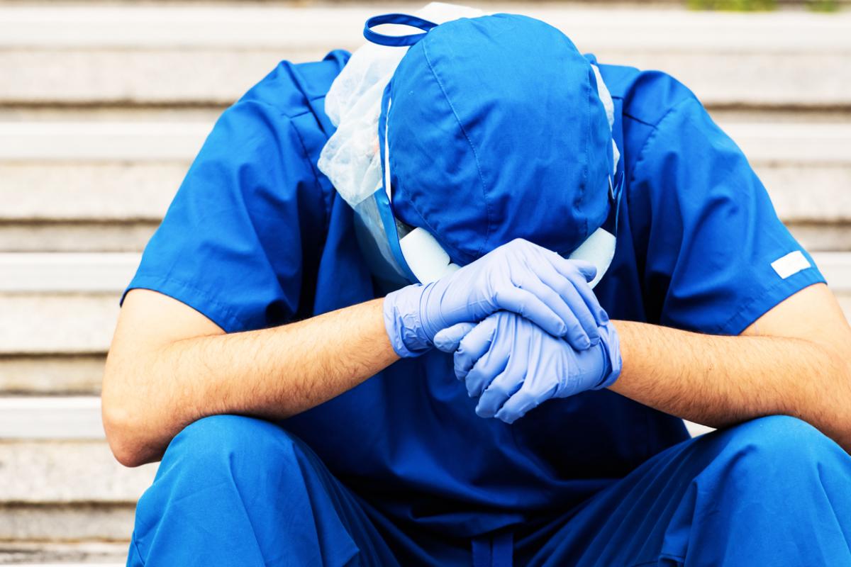 Exhausted health professional wearing PPE and sitting on steps with head down