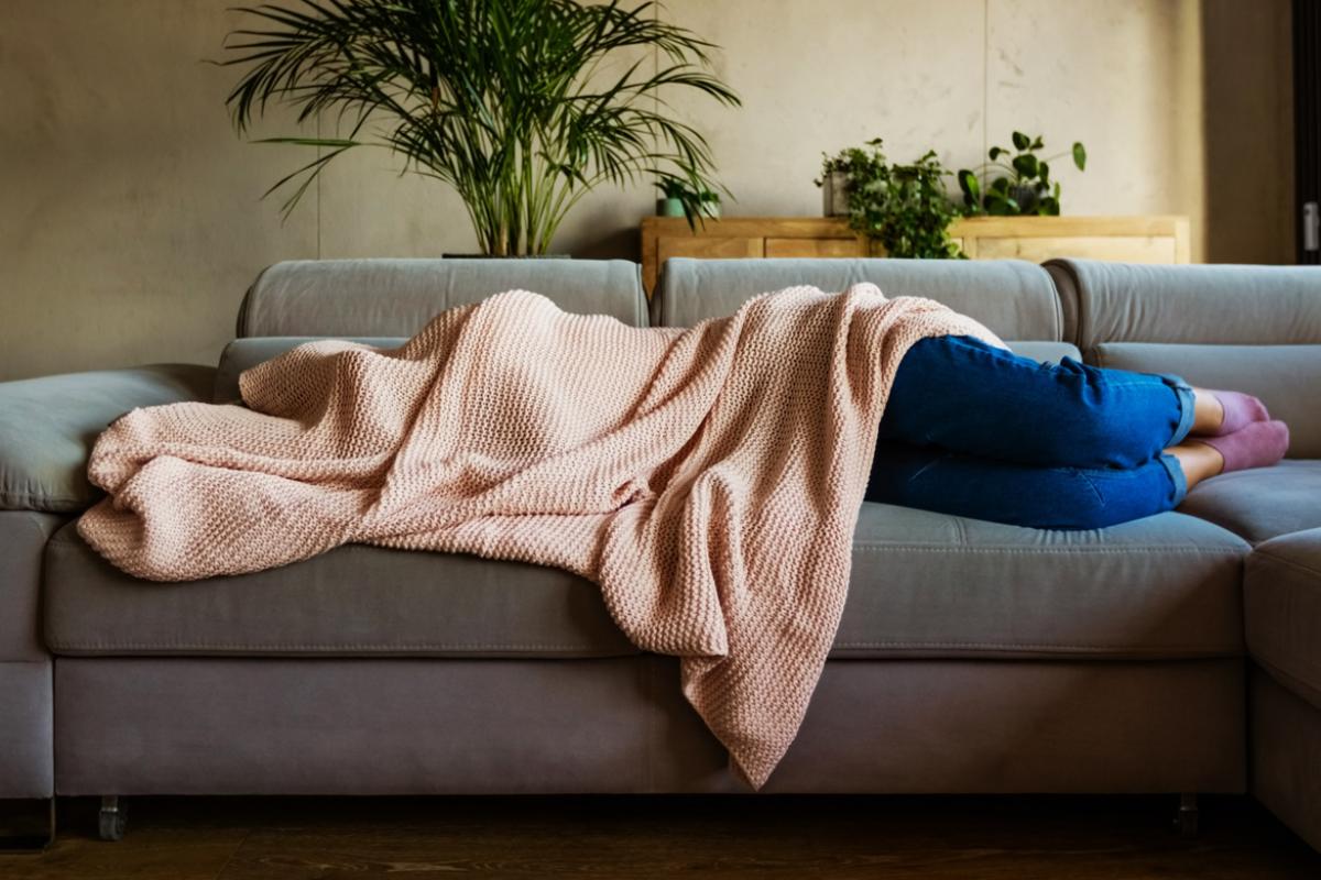 A woman covered with a blanket and sleeping on a sofa 