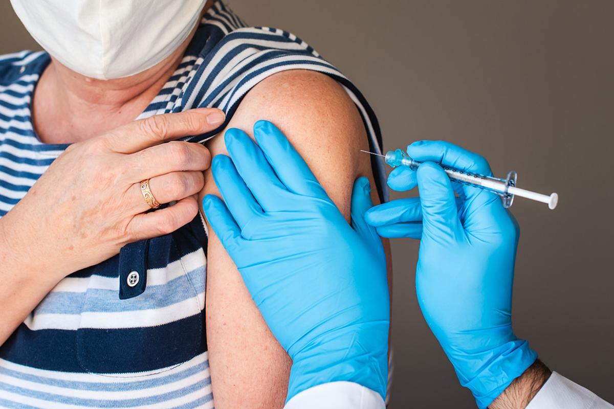 Tight shot of gloved health professional vaccinating masked person in left arm