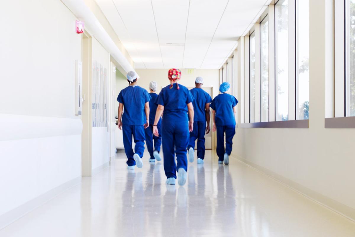 Back shot of five health professionals with scrubs walking down a hospital hallway towards the operating room