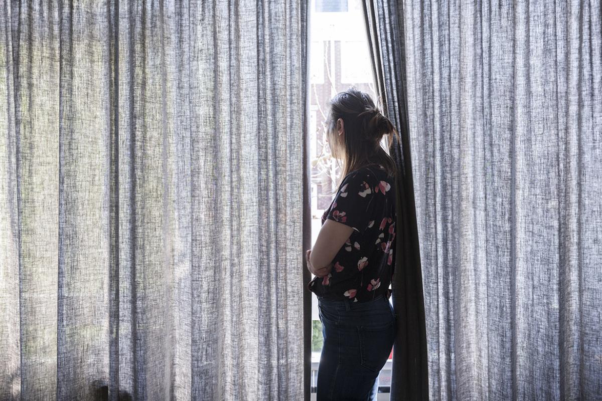 Side profile of woman staring out a curtained window