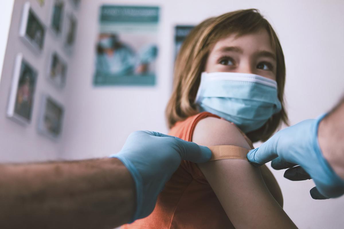 Health professional putting a plastic bandage on a little girl's arm after giving her a vaccination