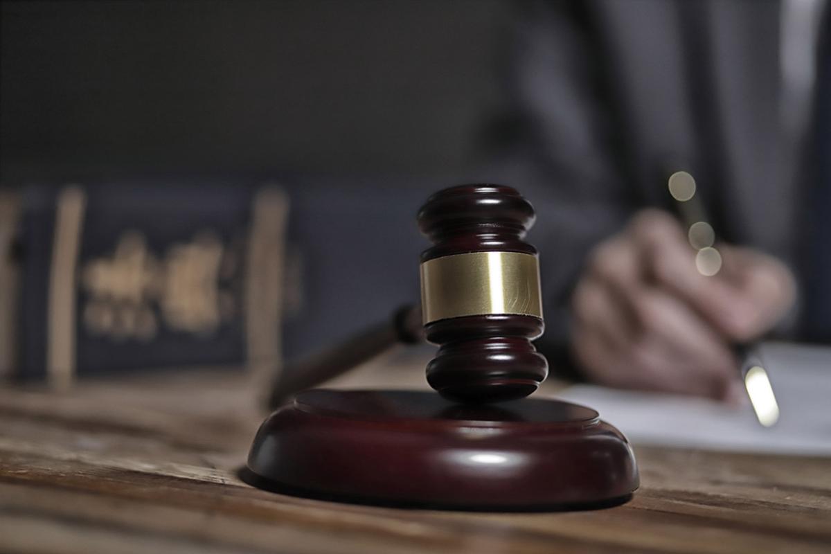 Tight shot of gavel on a desk with someone's hand in the background holding a pen