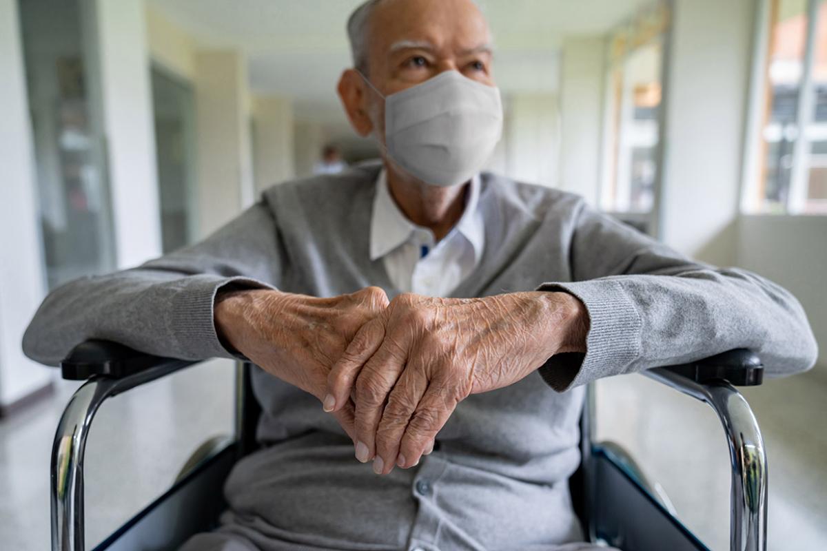 Elderly man wearing a mask and sitting in a wheelchair with his hands crossed