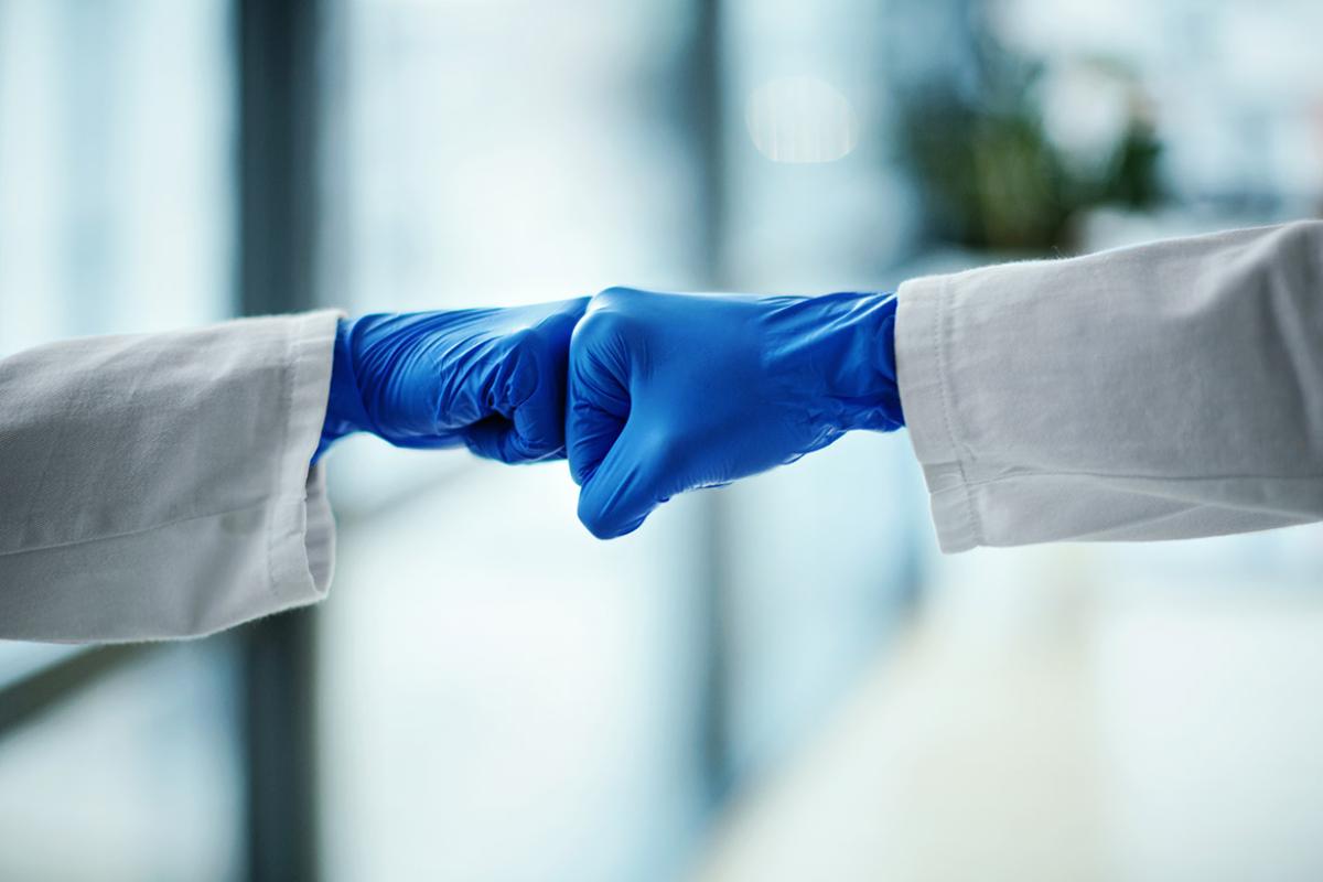 Tight shot of two health professionals wearing gloves giving each other fist bumps.