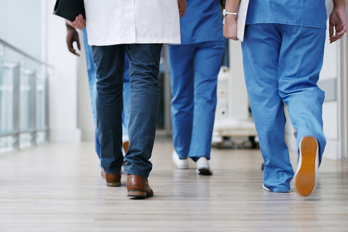 Tight shot of bottom legs of group of health professionals walking down a hospital hallway or corridor.
