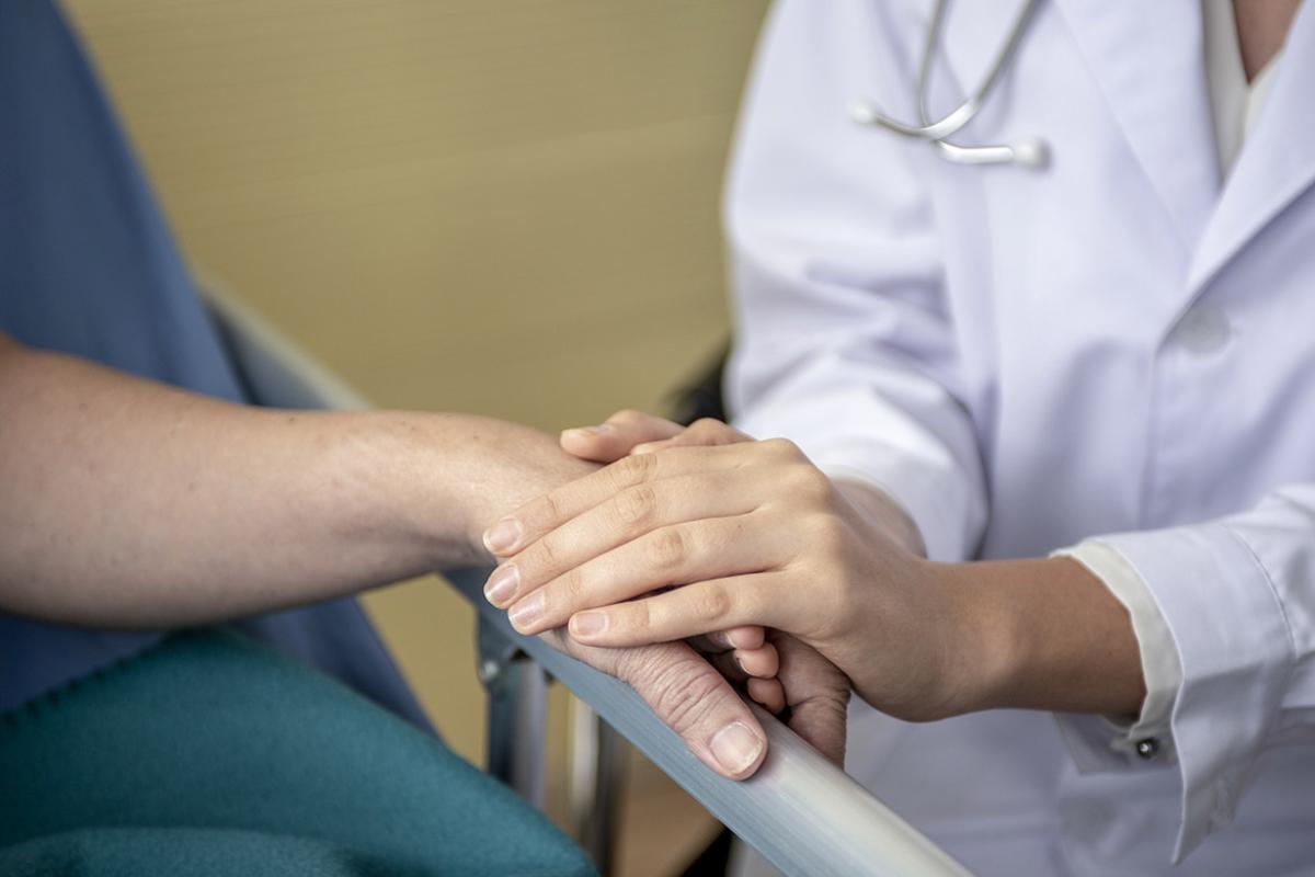 Tight shot of physician holding the hand of a patient laying on a hospital bed