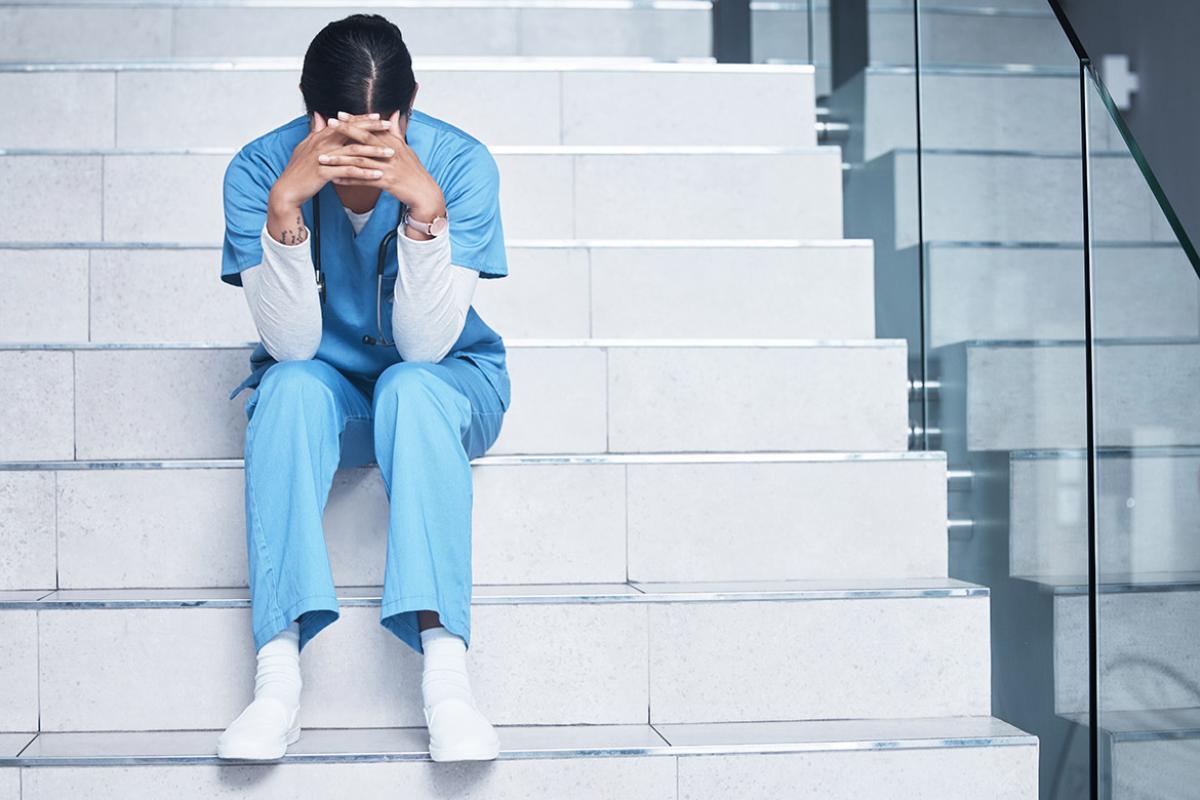 Exhausted or stressed health professional sitting on steps with elbows on knees, resting head between hands