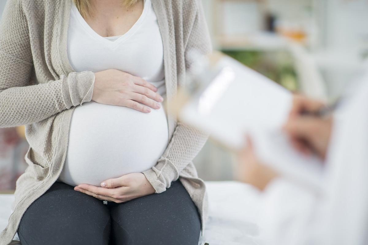 Pregnant woman holding her belly with two hands while consulting with a physician