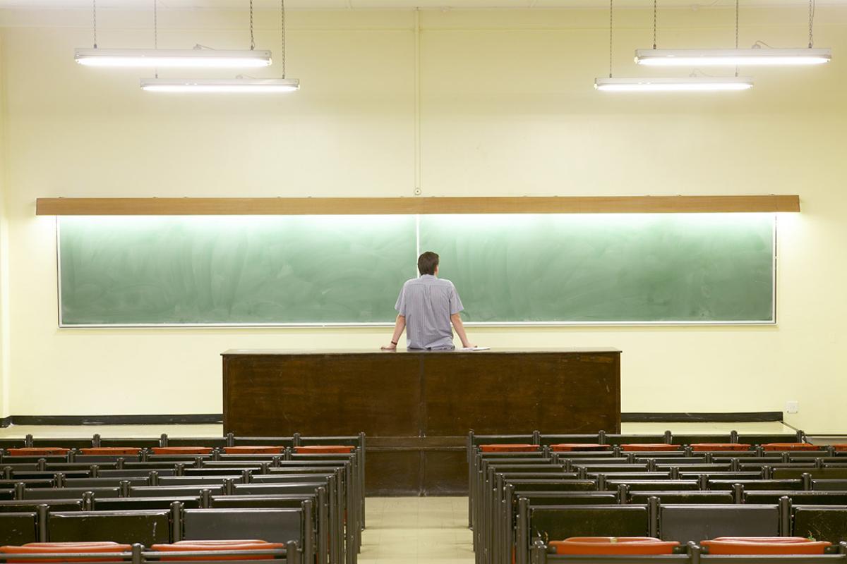 Professor standing in front of a chalk board with his back to an empty classroom